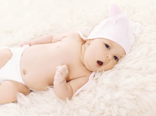 Sweet baby in hat yawns on the bed — Stock Photo, Image