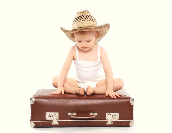 Ребенок в соломенной летней шляпе сидит на чемодане, деревенский хлев — стоковое фото