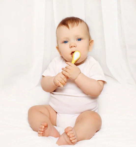 Baby mit Löffel sitzt zu Hause auf dem Bett — Stockfoto