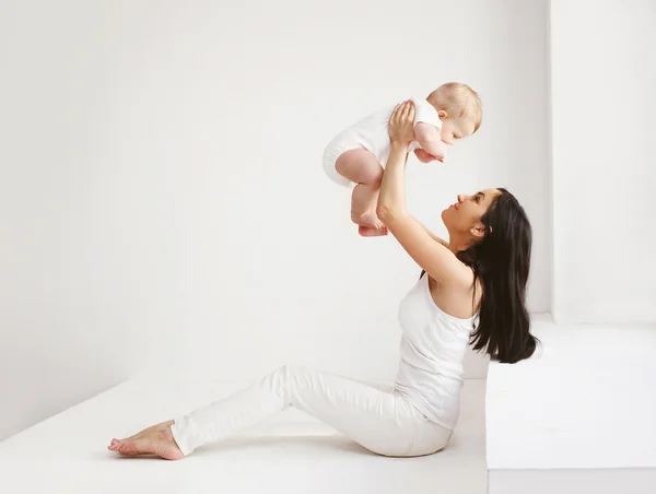 Gelukkig moeder en baby plezier samen op thuis in witte kamer — Stockfoto