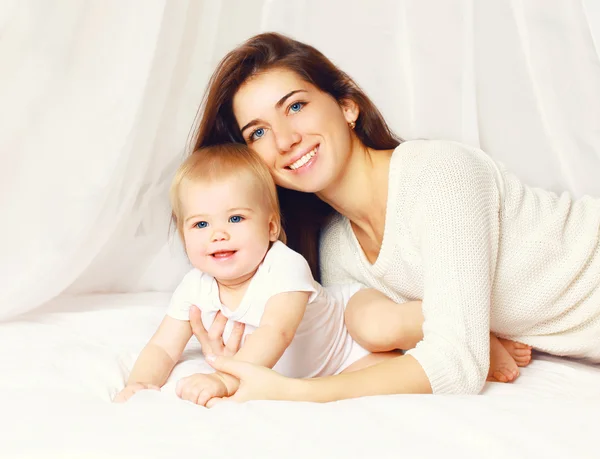 Portret van gelukkig lachend jonge moeder en schattige baby op het bed — Stockfoto