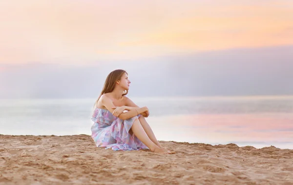 Jovem mulher sentada na praia na costa desfrutando do pôr do sol do mar — Fotografia de Stock