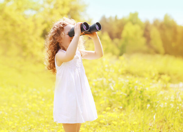 Sunny photo child looks in binoculars outdoors in warm summer da