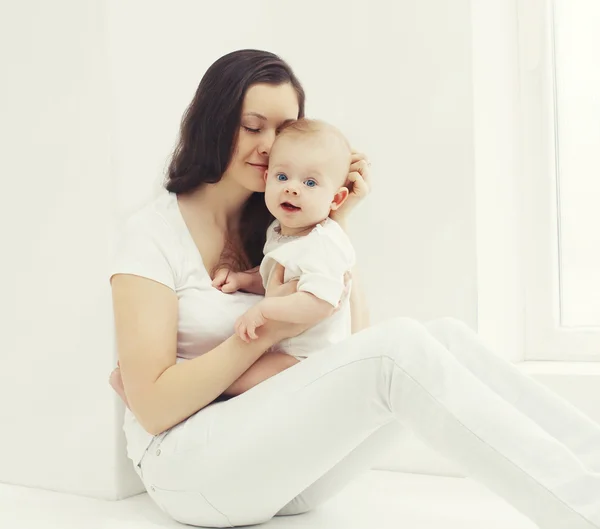 Feliz foto joven madre con el bebé en casa en habitación blanca cerca de wi —  Fotos de Stock