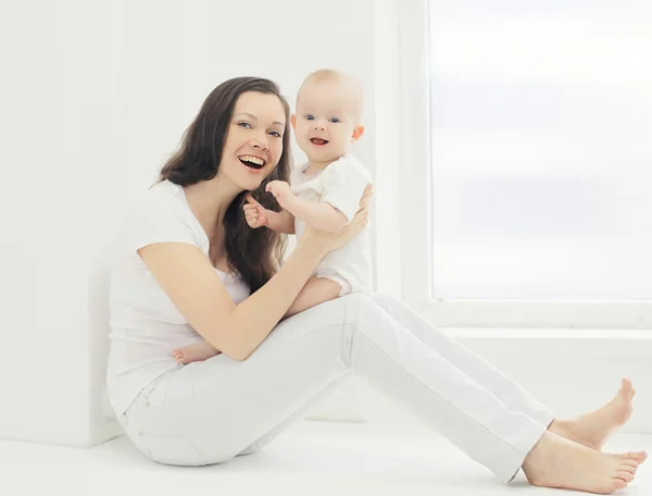 Šťastný mladý usmívající se matka s dítětem doma v bílé místnosti nedaleko — Stock fotografie