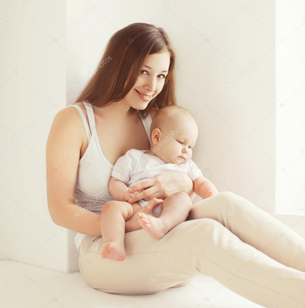 Happy young mother with baby together at home in white room near