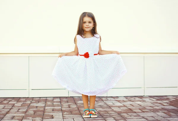 Belle petite fille montre robe blanche à l'extérieur contre l'urb — Photo