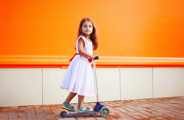 Lilla flickan i klänning på skoter mot väggens färgglada — Stockfoto