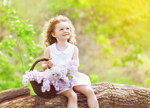座っていると、su を楽しんでいるライラックの花のバスケットを持つ少女 — ストック写真