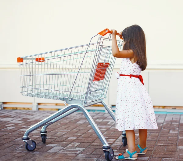 Little girl with shopping cart outdoors near shop — Stock Photo, Image