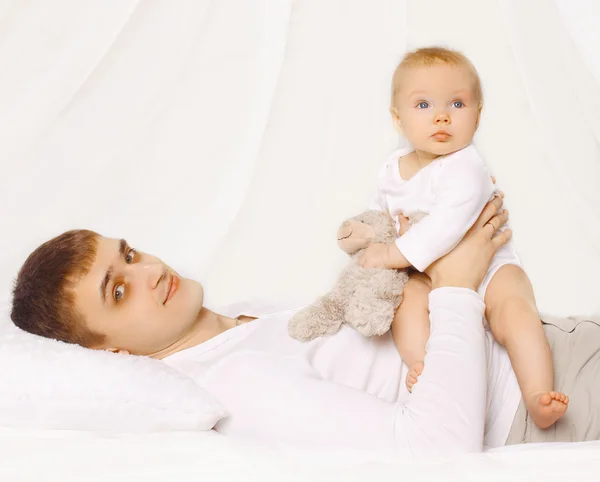 Vater und Baby zu Hause liegen zusammen auf dem Bett, Kind spielt — Stockfoto