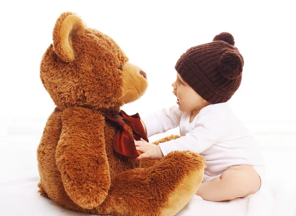 Bebé en sombrero marrón de punto jugando con oso de peluche grande —  Fotos de Stock