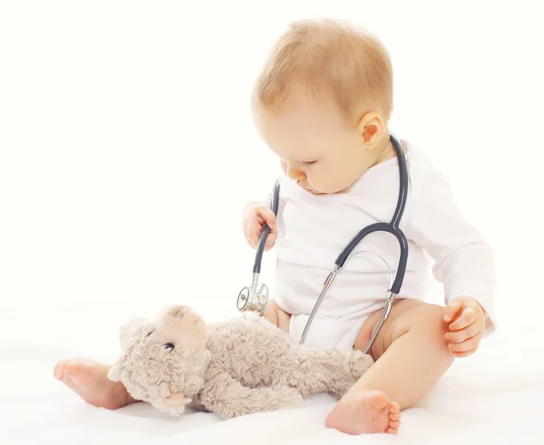 Baby spielt und hört Stethoskop-Teddybär Stockfoto