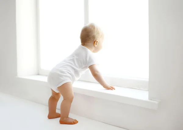 Lindo bebé en casa en la habitación blanca está cerca de la ventana —  Fotos de Stock