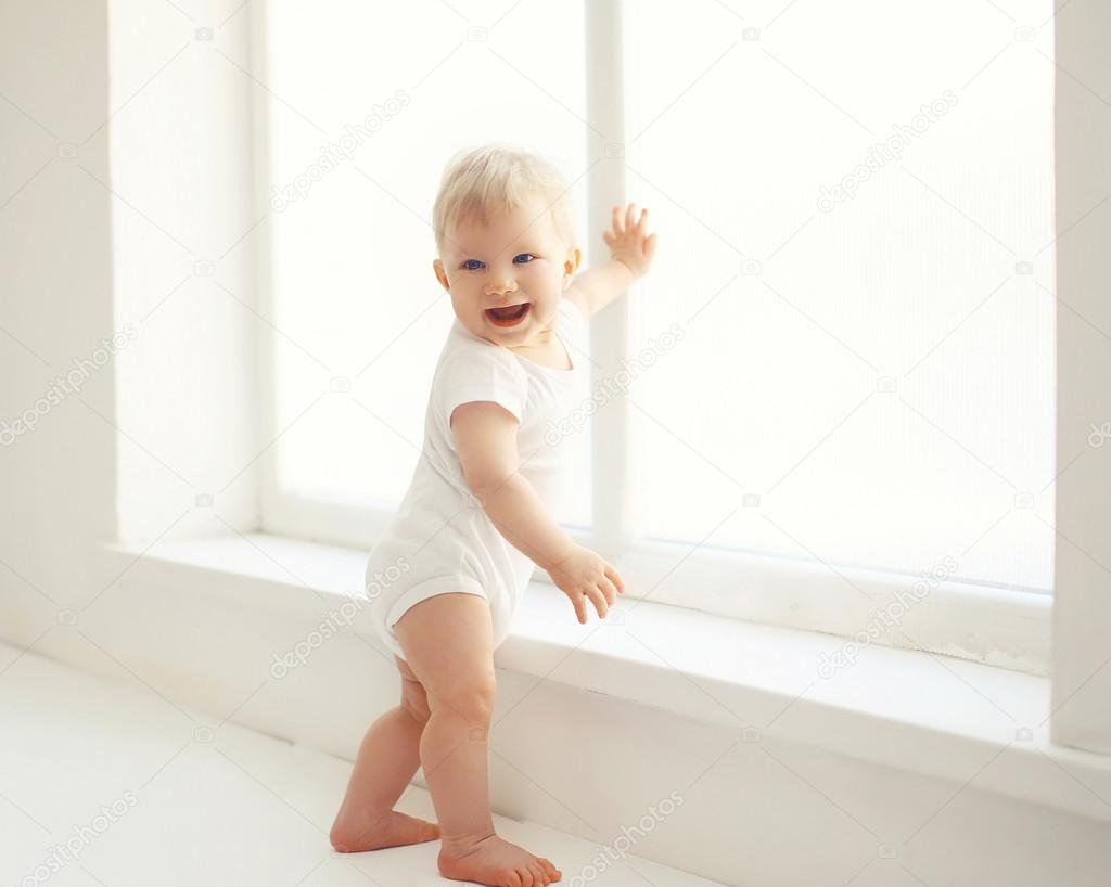 Smiling baby standing in white room at home near window
