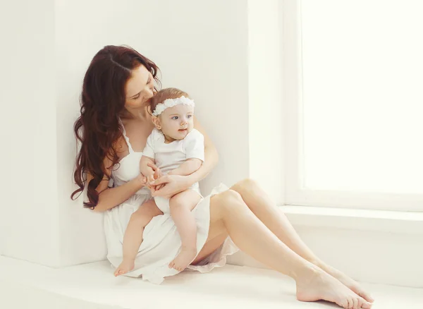 Gelukkig jonge moeder en baby samen thuis in witte kamer in de buurt van — Stockfoto