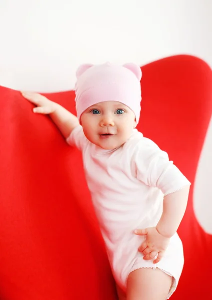 Baby in hat standing on the armchair at home — Stock Photo, Image