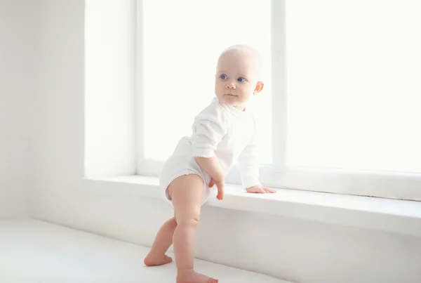 Pequeño bebé jugando cerca de la ventana en la habitación blanca —  Fotos de Stock