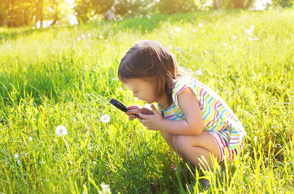 Little child looking through a magnifying glass on dandelion flo