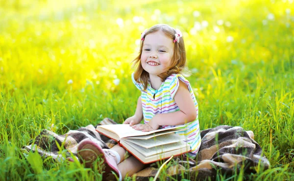 Portrait of little smiling girl child with book sitting on the g — Stock Photo, Image