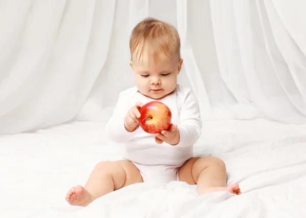 Retrato de bebé sentado con manzana roja en la cama en casa —  Fotos de Stock