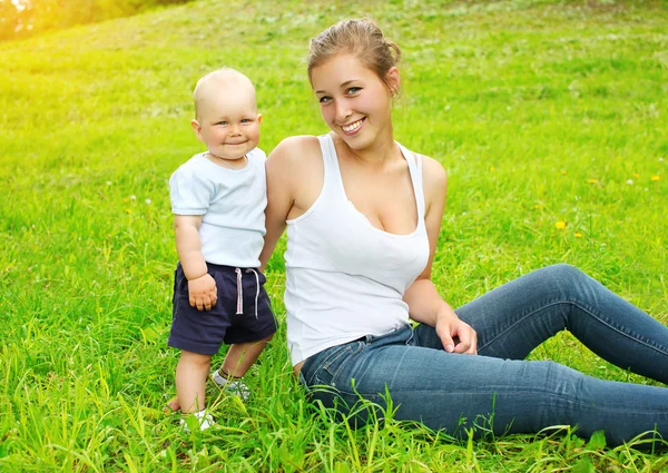 Счастливые улыбающиеся мать и сын ребенка, сидя на траве в сумме — стоковое фото