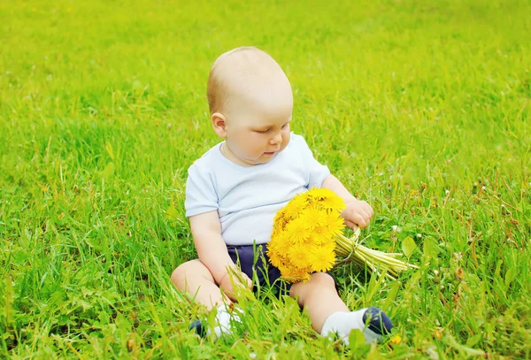Ritratto di bambino con fiori di tarassaco gialli seduto sul gr — Foto Stock
