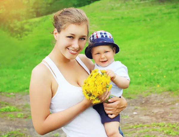 Portrait of happy mother and baby with yellow dandelion flowers — Stock Photo, Image
