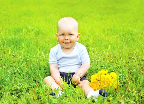 Porträtt av söt baby med gula maskros blommor sittande på t — Stockfoto