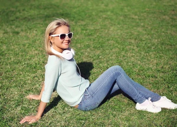 Young pretty smiling girl sitting on the grass listens to music — Stock Photo, Image