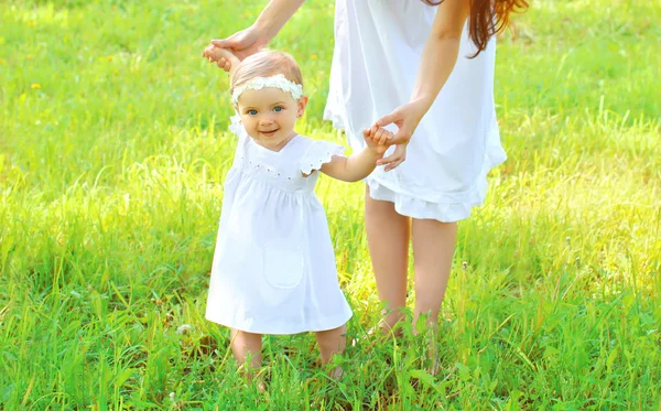 Mãe de mãos dadas bebê andando juntos na grama em ensolarado — Fotografia de Stock
