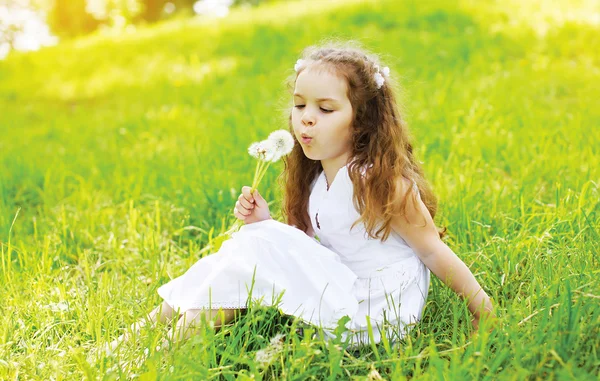 Retrato de criança menina na grama soprando dandeli branco — Fotografia de Stock