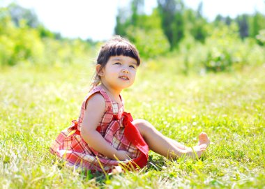 Little girl child sitting on the grass outdoors enjoying warm su