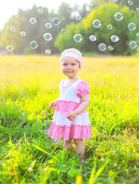 Cute little child on the grass with many soap bubbles in sunny s