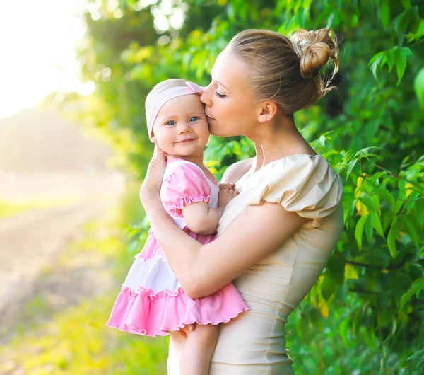 Retrato de mãe abraço e beijando bebê filha ao ar livre ao sol — Fotografia de Stock