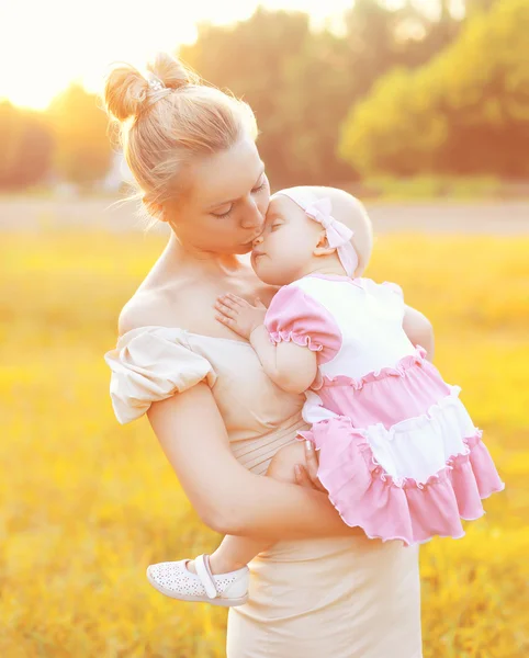 Sunny portrait of happy mom kissing baby on hands in sunny eveni — Stok fotoğraf