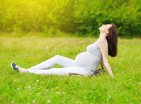Счастливая беременная женщина сидит на траве и наслаждается солнечной суммой — стоковое фото