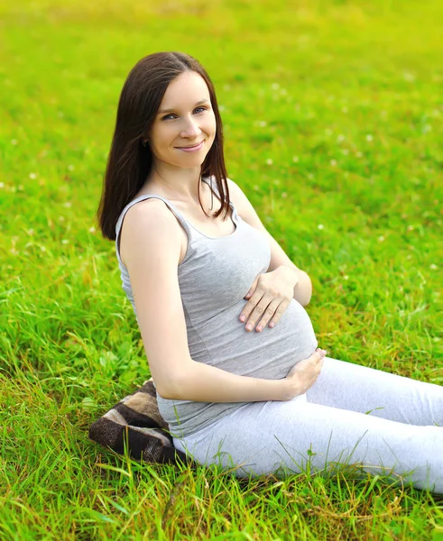 Happy smiling pregnant woman sitting on the grass in summer day — Stockfoto