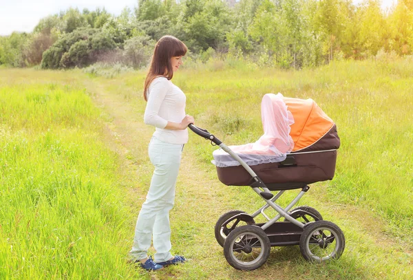 Happy young mother walking with baby stroller outdoors on the na