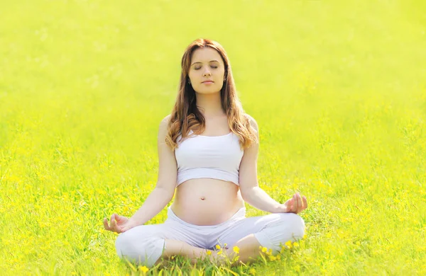 Těhotná žena sedí na trávě, děláte cvičení jógy v sunny — Stock fotografie