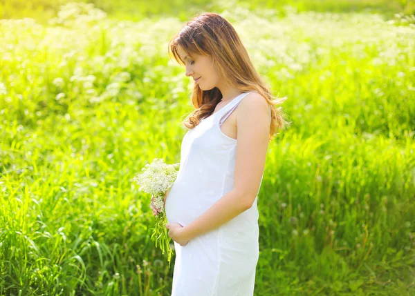Zonnige foto van mooie jonge zwangere vrouw in witte jurk wit — Stockfoto