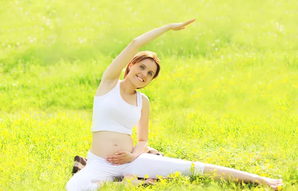 Беременная женщина, сидящая на траве и занимающаяся фитнесом или йогой — стоковое фото