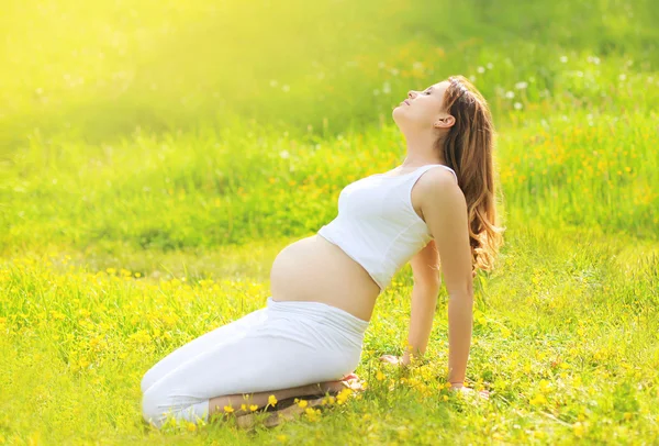 Беременная женщина на траве занимается йогой и наслаждается солнечным — стоковое фото