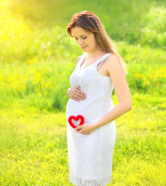 Unga gravid kvinna med rött hjärta utomhus i solig sommardag — Stockfoto