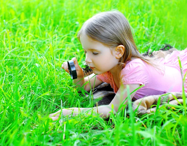 Malá dívka dítě dívat se skrz zvětšovací sklo na gras — Stock fotografie