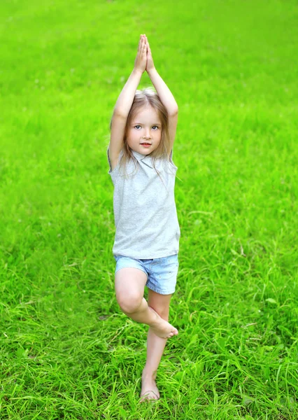 Kleines Mädchen auf dem Gras macht Yoga-Übungen im Freien in su — Stockfoto