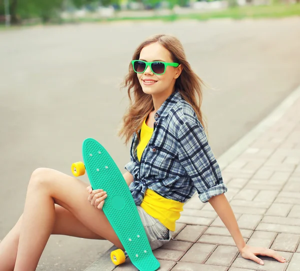 Portrait of smiling pretty cool girl in sunglasses with skateboa