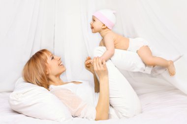 Happy mother playing with baby having fun together on the bed at