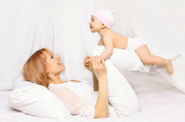 Happy mother playing with baby having fun together on the bed at — Stockfoto