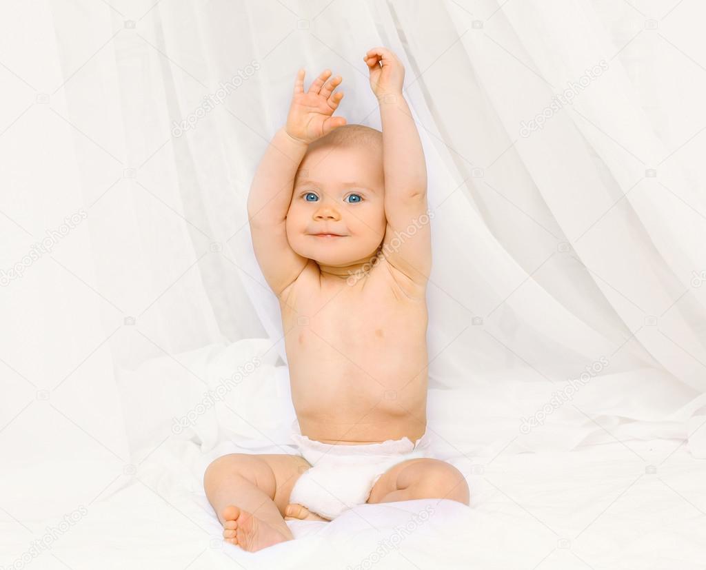 Portrait of happy active baby in diapers playing on the bed at h